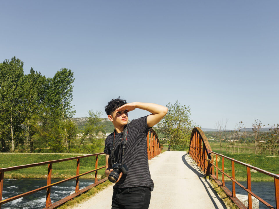 Young man with a camera on a sunny bridge